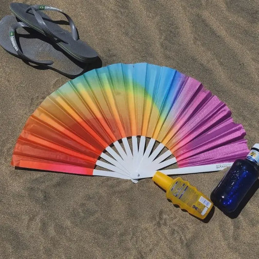 Colorful fan on sand with flip-flops and bottles nearby